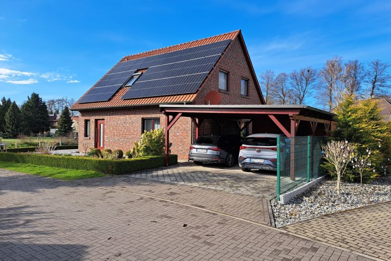Kleines Einfamilienhaus mit großer Solaranlage und zwei Autos in einem Carport am Haus.